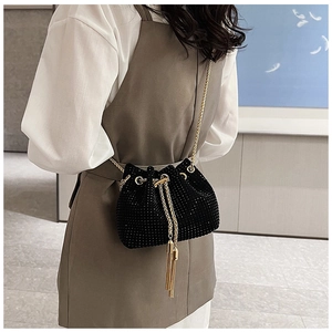 Detail of a black rhinestone bucket bag featuring gold chain and tassel on a model
