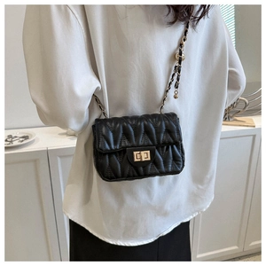 Detail of black quilted shoulder bag with gold twist lock and chain strap on a white shirt