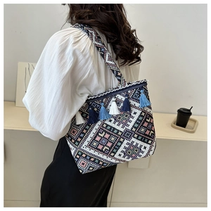 Ethnic woven tote bag with geometric patterns and colorful tassels shown on a model