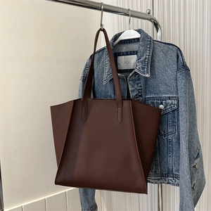 Detalle del bolso tote marrón oscuro con laterales de ala y chaqueta vaquera