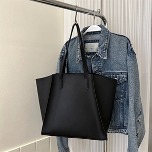Detalle de un bolso tote negro mate minimalista colgado junto a una chaqueta vaquera