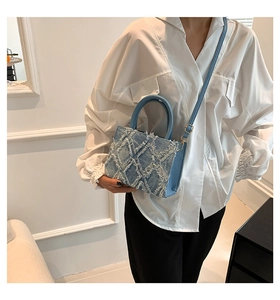 Detail of light blue denim handbag featuring frayed tassel patchwork and adjustable strap