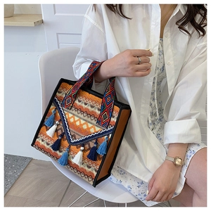 Dettaglio della borsa tote bohémien in tela arancione con manici intrecciati e nappe con frange
