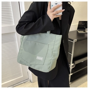 Detail view of the sage green nylon tote bag featuring a front pocket and fashion label