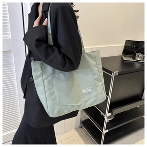 Detail of light green nylon tote bag featuring front pocket and minimalist fashion tag