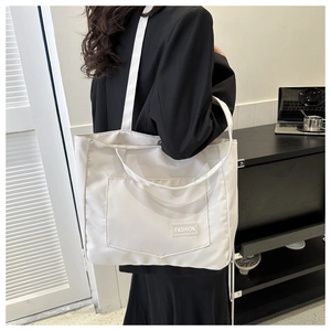 Detailed side view of white nylon tote bag with front pocket and fashion label on shoulder