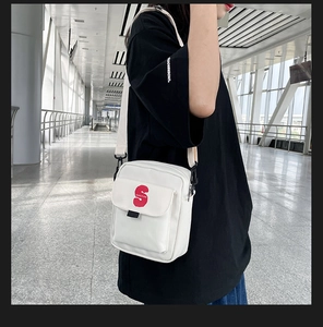Detalle de bolso bandolera blanco con letra S roja degradada y correa de nailon