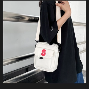Detalle de bandolera de lona blanca con logotipo S rojo y correa de tela