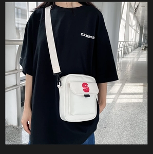 Detalle del bolso bandolera de nailon blanco con estampado S rojo, mostrado en modelo