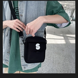 Detalle del bolso bandolera de lona negra con un llamativo estampado de la S blanca en la solapa