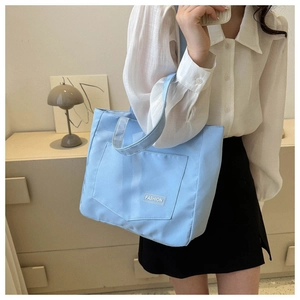 Detail of light blue canvas tote bag with front pocket and white FASHION label