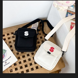 Detalle de bolsos bandolera de lona minimalistas en negro y blanco roto con el logo S