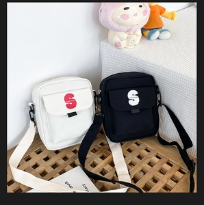 Detalle de bolsos bandolera de lona en negro y beige con estampado de letra S en banco