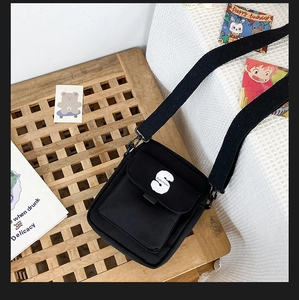 Vista detallada del bolso bandolera de nailon negro con logo S blanco en mesa de madera