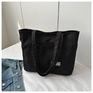 Detail of a black nylon tote bag with a front pocket and white Fashion brand tag