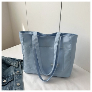 Detail of light blue nylon tote bag with fashion label and front pocket feature