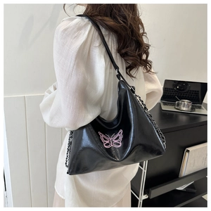 Detail van zwarte PU-schoudertas met roze vlinderborduurwerk en zilveren kettingriem