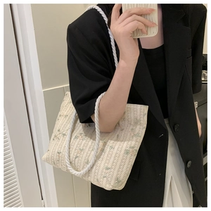 Detail of floral woven straw tote bag with chunky white rope handle and cotton texture