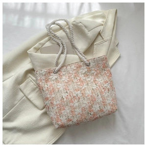 Close-up of floral lace tote bag fabric with woven rope handles on tweed background