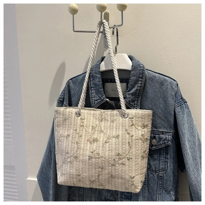 Detail of floral embroidery on a beige woven tote bag with white rope handles