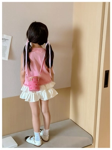 Détail du sac seau rose avec motif cerise porté par un enfant en gilet tricoté