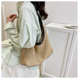 Detail view of woven straw tote bag with black leather trim worn on shoulder by model