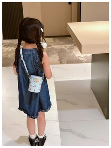 Détail d'un mini sac seau bleu à motif cerises porté par une fille en robe denim
