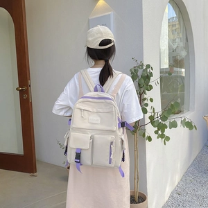 Detail view of cream campus backpack with multiple pockets and purple straps on a model