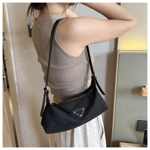 Model wearing a black nylon hobo shoulder bag with a metal triangle logo detail