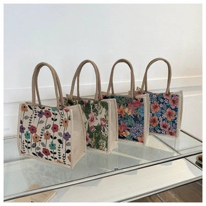 Detailed view of four printed canvas tote bags with woven handles on a glass table