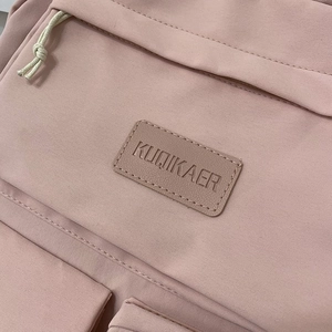 Detail showing pink polyester backpack with branded leather logo and beige zipper pullers