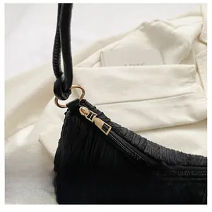 Detail of a black pleated shoulder bag showing the smooth golden zipper and knot strap