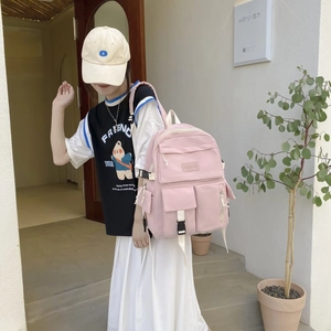 Close-up of pink multi-pocket backpack with cream straps and plastic buckles worn by model