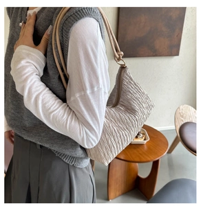 Detail of beige pleated shoulder bag with slim strap and metallic ring hardware