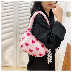 Detail of pink plush tote bag with red hearts worn by a model in a casual setting