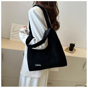Détail d'un sac cabas en velours côtelé noir avec étiquette Fashion porté par mannequin