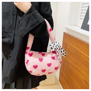 Close-up of pink plush handbag featuring red heart patterns and a polka dot ribbon detail