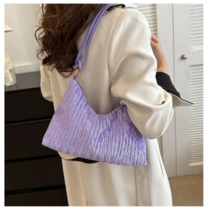 Detail of purple pleated underarm bag showing textured fabric and golden metal rings