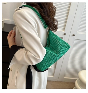 Side view of a green pleated cloud-shaped underarm bag worn on a shoulder