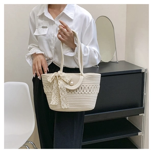 Detail of cream woven handbag featuring wave textures, a pearl clasp, and lace bow