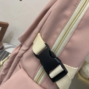 Detail of a pink school backpack featuring a black side buckle and cream nylon webbing