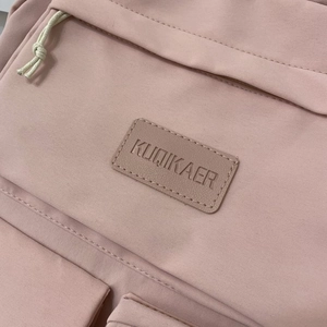 Close-up of pink canvas backpack featuring a leather brand logo and white zipper knots