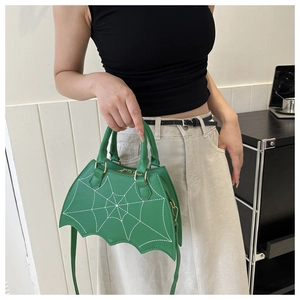 Detail der grünen Handtasche in Fledermausform mit weißem Spinnennetzmuster und Griffen