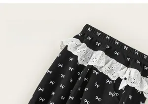 Close-up of girls' black cotton trousers featuring bow prints and white lace waistband details