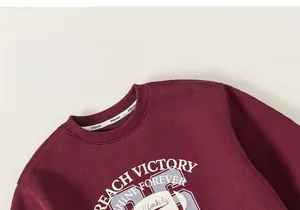 Detailed view of the neckline and white letter printing on burgundy long sleeve sweatshirt
