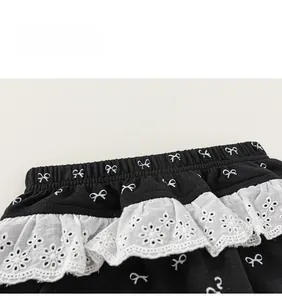 Detail of girls' black trousers featuring bow print and white embroidered lace waist