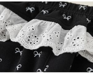 Detailed view of kids' black knit pants featuring white bow prints and delicate lace edging