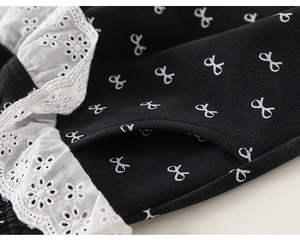 Close-up of black children's pants showing white bow prints and delicate lace pockets