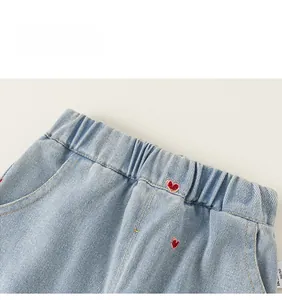 Gros plan d'un jean enfant bleu clair avec taille élastique et broderie cœur rouge