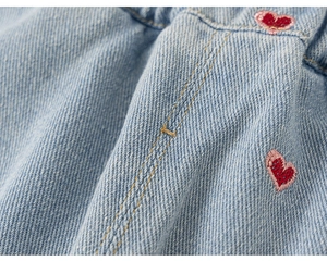 Détail de la broderie cœur rouge et des coutures jaunes sur le jean bleu pour filles